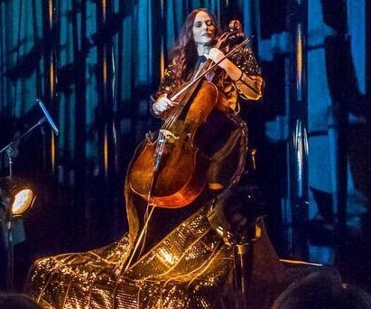 A musician plays the cello in a room with a dark background.